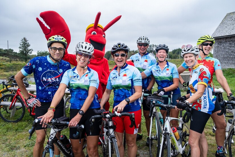 Une photo de 7 cyclistes avec la mascotte du homard lors d'une pause pendant le Gran Fondo Baie Sainte-Marie.